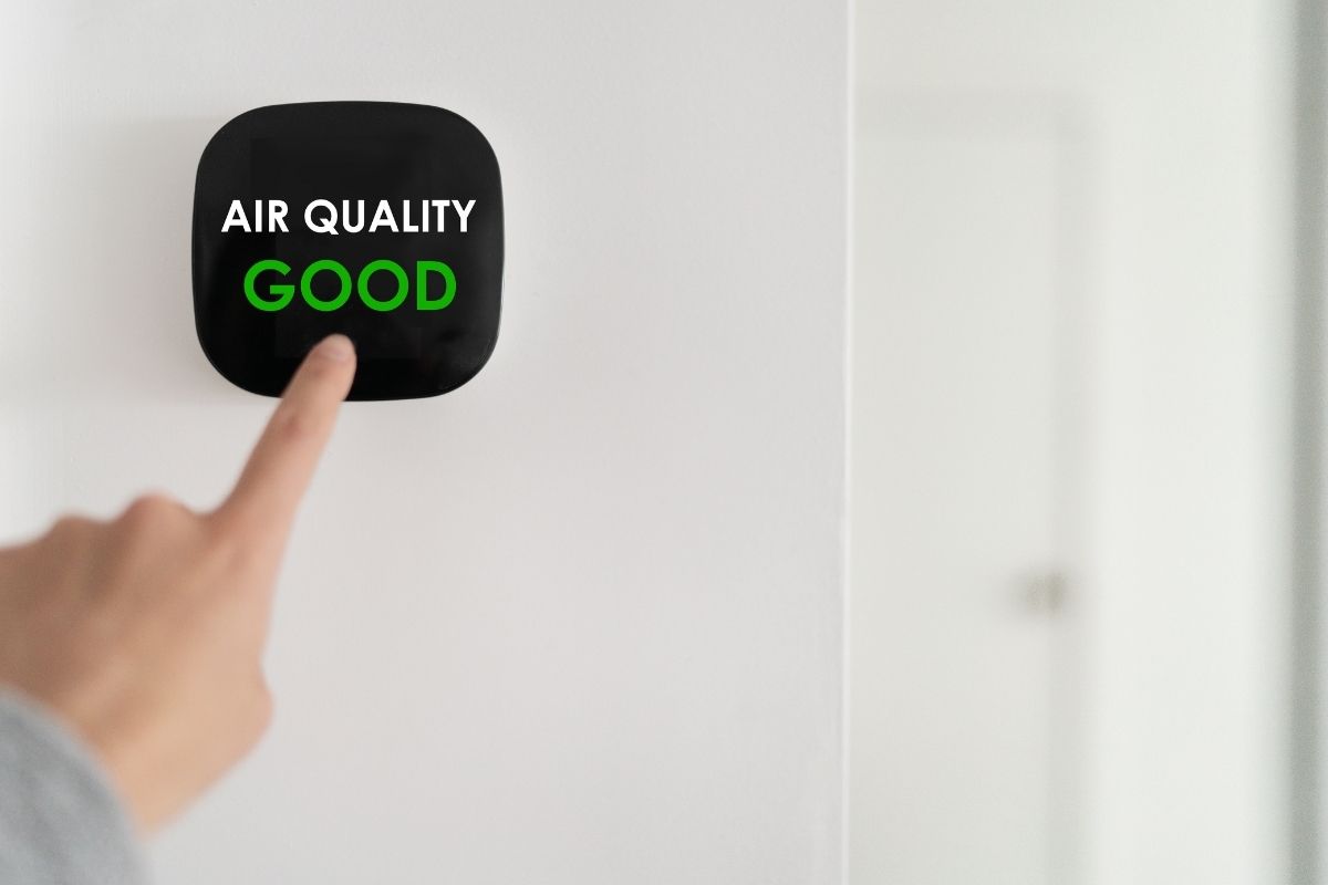 close shot of a hand touching the air quality testing gadget. "Air Quality Good" written on the screen of gadget.