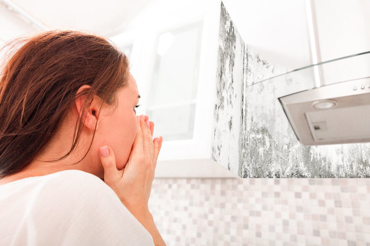 a woman looking worried after seeing black mold on the wall.