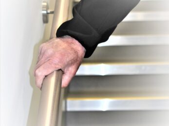 An old man grips a sanitized handrail