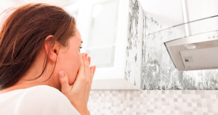a woman looking worried after seeing black mold on the wall.